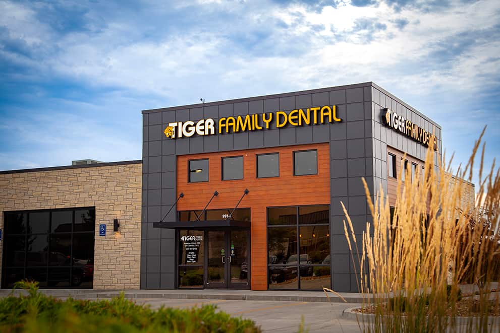 The image shows a modern building with a sign reading TIGER FAMILY DENTAL on the front, indicating it s a dental clinic.