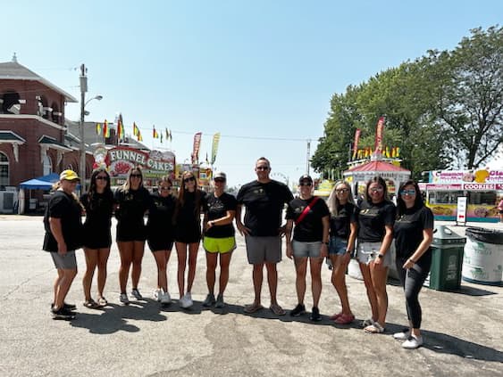 A group of people posing together outdoors during the daytime, with some standing in front of a sign.