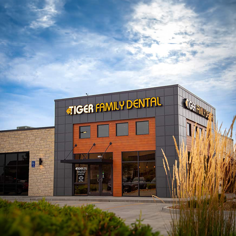 The image shows a building with a sign that reads TIGER FAMILY DENTAL in front of a clear sky background.