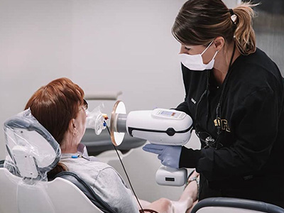 The image shows a dental hygienist assisting a patient during a dental appointment, with the dental hygienist using an ultrasonic scaler on the patient s teeth.
