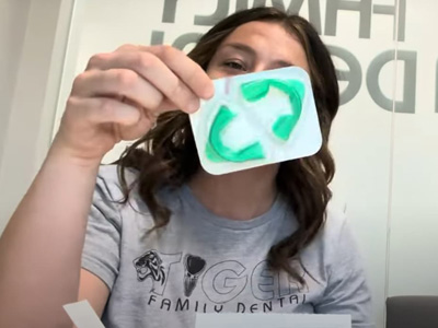 A woman holding up a green toothpaste tube with a white swirl design.