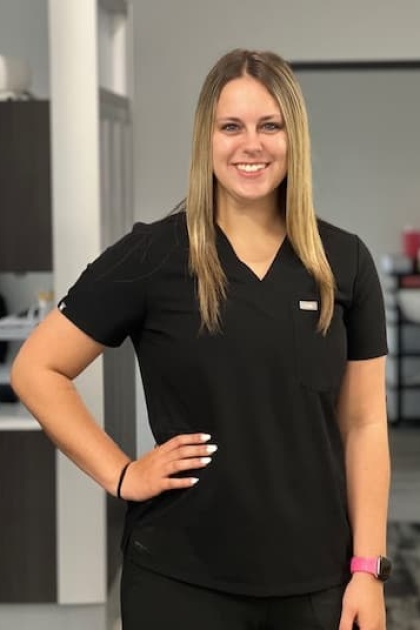 The image shows a woman wearing a black polo shirt with white stripes on the sleeves, standing indoors with a smile, posing for a photo.