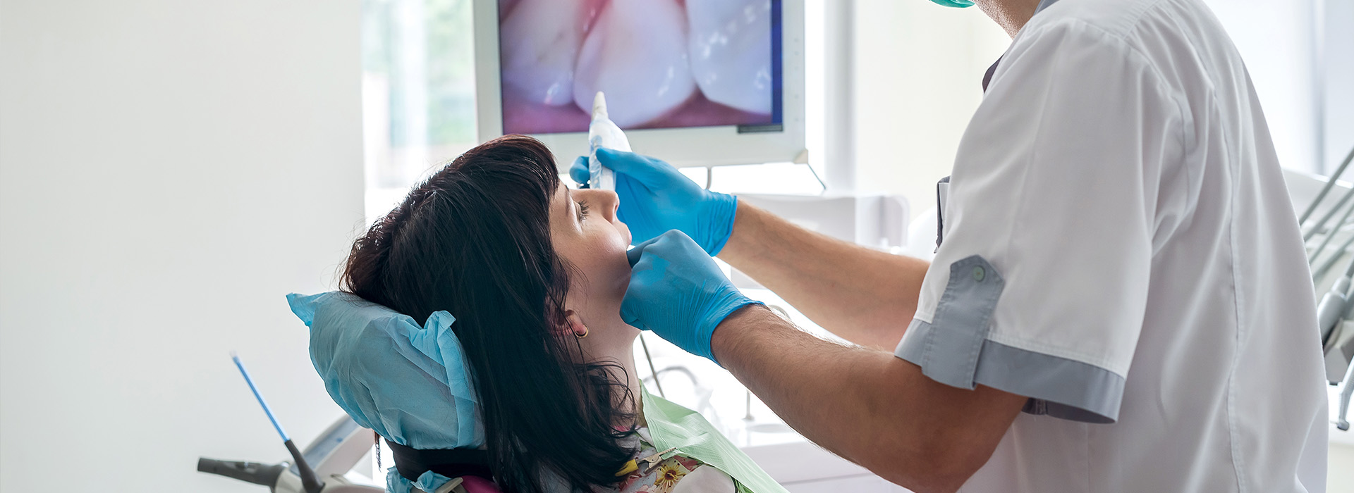 The image shows a professional dental setting with a dentist performing a procedure on a patient s mouth while wearing protective gloves, with a focus on the dentist s hands and the patient s mouth area.
