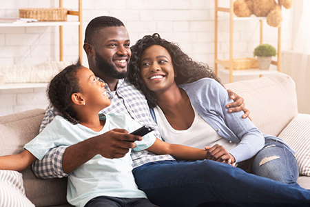 A family of four posing together on a couch with a warm expression, featuring two adults and two children.