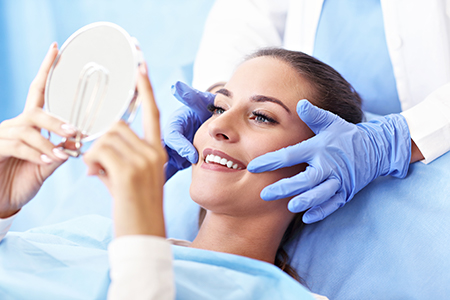 This image depicts a person receiving a facial treatment at a dermatology clinic, with a medical professional applying a device to their face while holding up a magnifying mirror.
