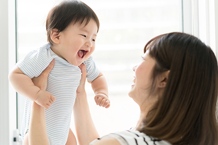 A woman holding a baby with a joyful expression, both indoors.