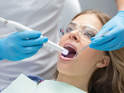 The image depicts a dental professional using an electronic device to clean a patient s teeth during a dental appointment.